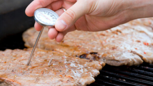 Hand inserting thermometer in meat