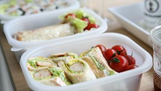 packed lunch items sandwiches and fresh tomatoes in plastic tupperware