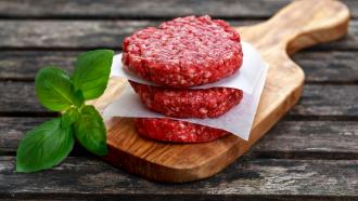 stacked raw beef burgers on a wooden cutting board