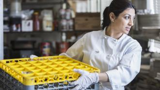 employee using a mechanical dishwasher in a commercial kitchen