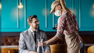Server wearing mask putting down bottle of water at table