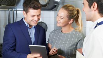 Training manager and staff in a kitchen, looking at a tablet.