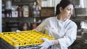 employee using a mechanical dishwasher in a commercial kitchen