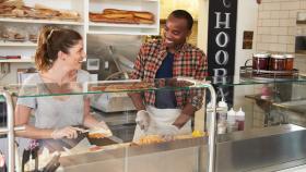 A man trains a woman on how to prepare food in a bakery.